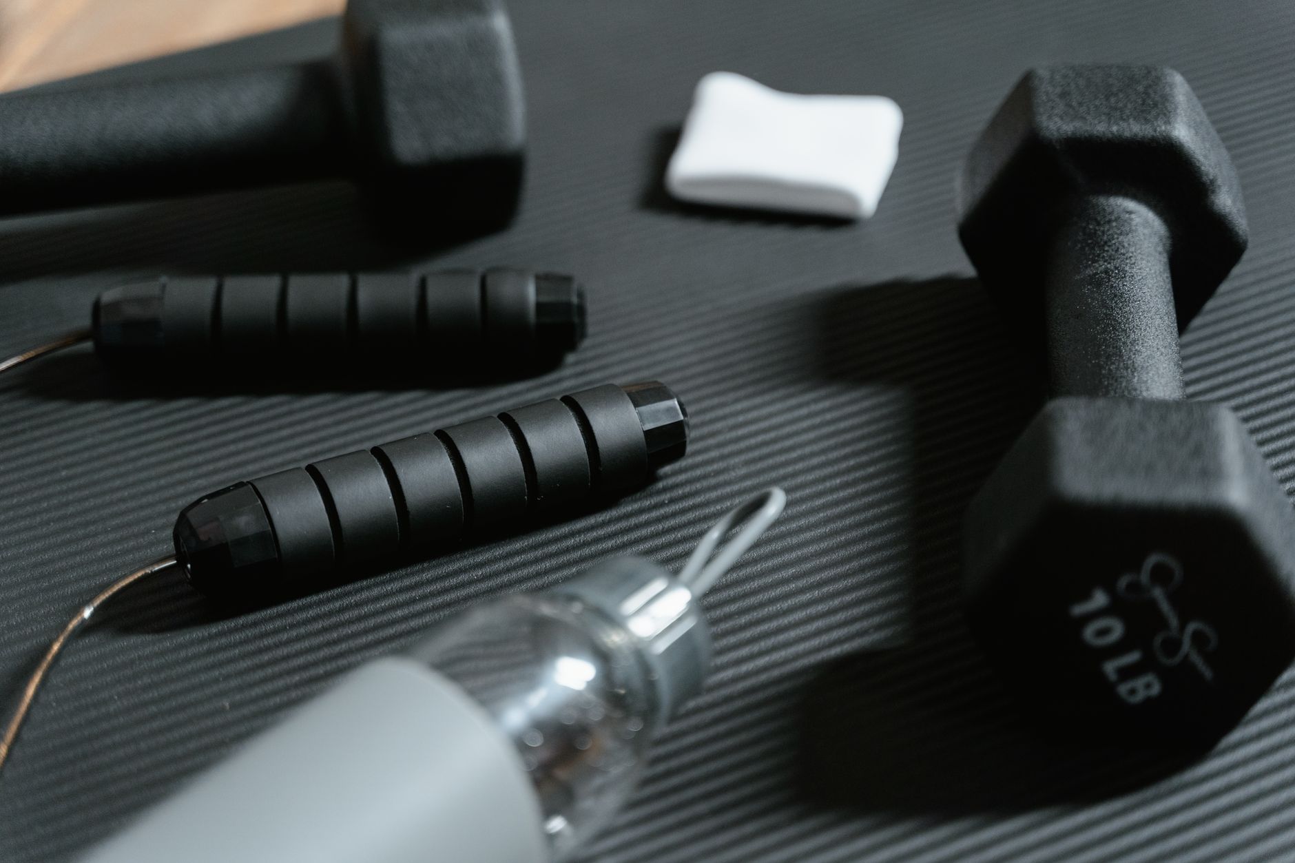 Dumbbells, jumping rope, and water bottle on a yoga mat for home workout routine. — Avoid Hip Bursitis Surgery - Go for Regen