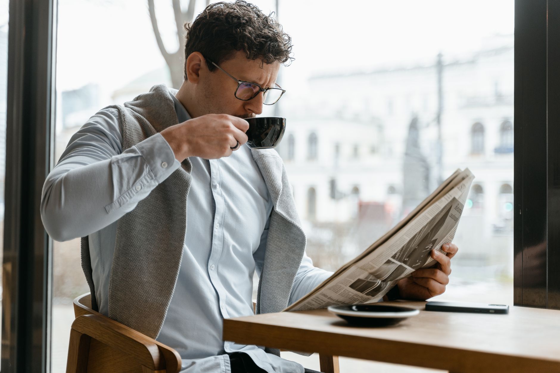 Adult man wearing eyeglasses sipping coffee and reading a newspaper in a cozy cafe setting. — Beef Casino: Die Wahrnehmung de