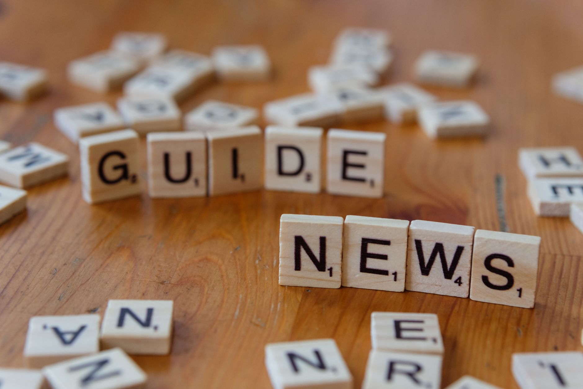 Close-up of Scrabble tiles spelling 'Guide' and 'News' on a wooden surface. — Comment profiter au mieux des freebies offerts