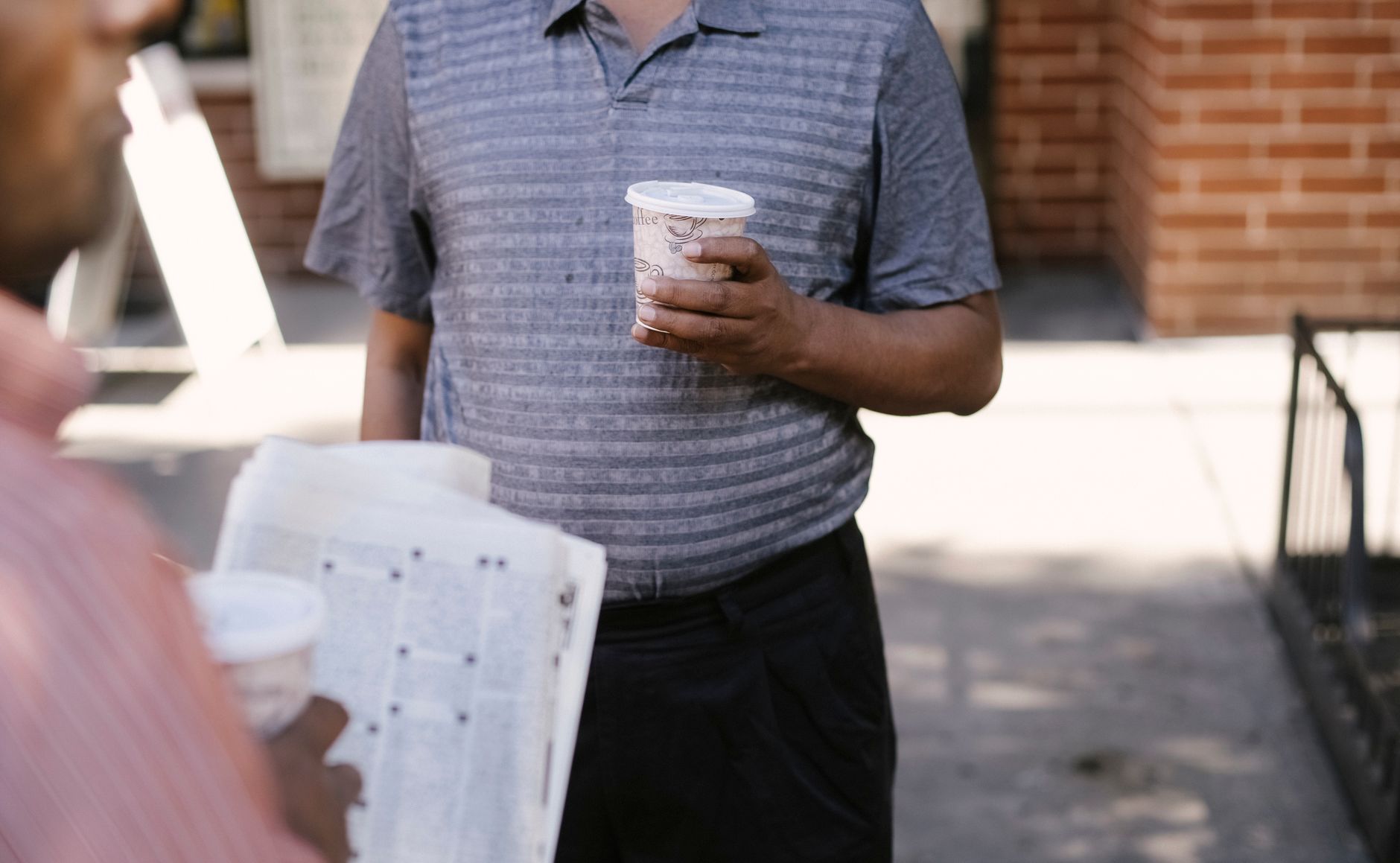 Crop anonymous ethnic male friends with coffee to go and newspaper speaking on city pavement — Die besten Spiele im Cat Casin