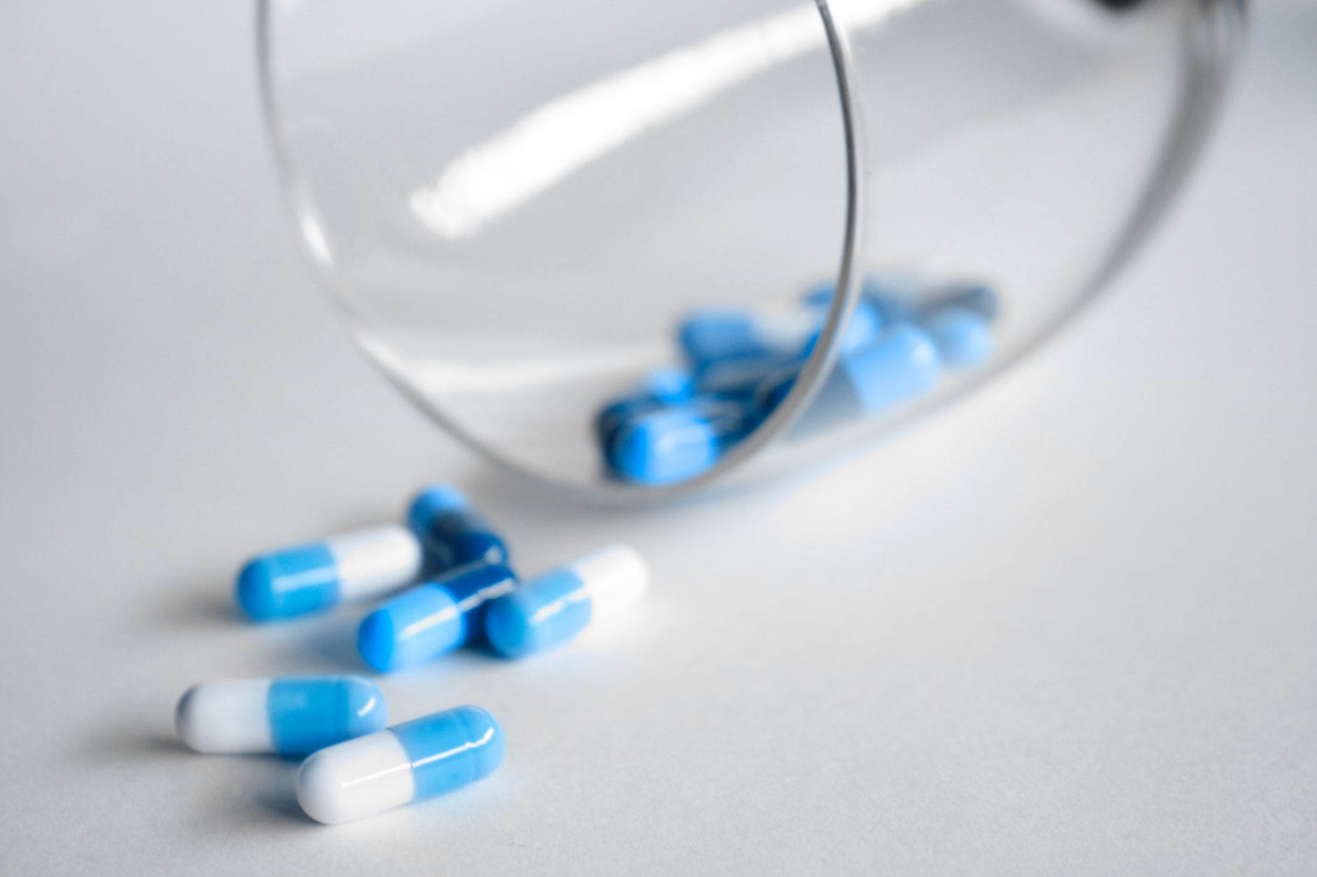 A close-up of blue and white capsules spilling from a glass on a light background. — How Dermal Fillers in Pittsburgh Will Ma