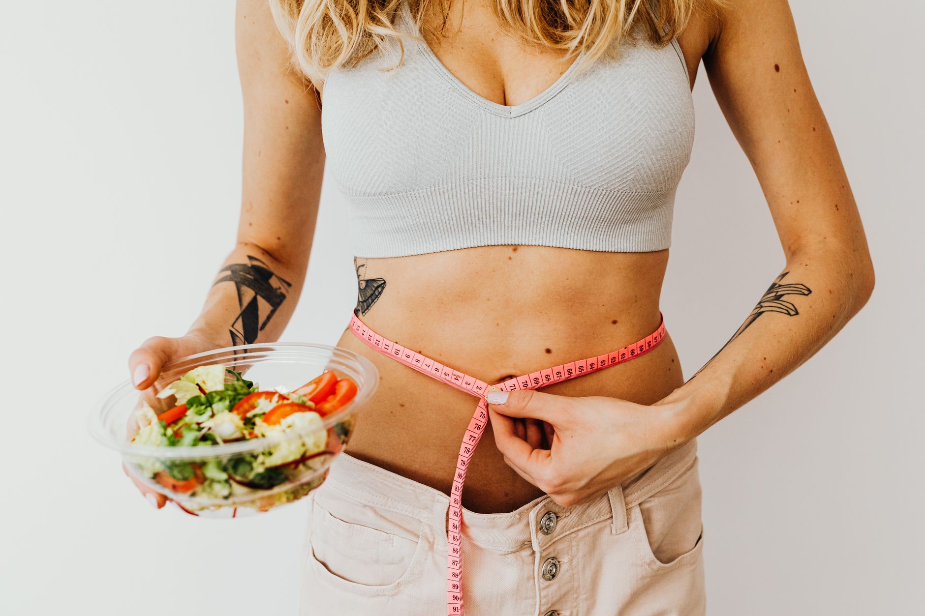 Woman measuring waistline while holding a fresh vegetable salad, emphasizing healthy living. — Kinds of Periodic Allergic rea