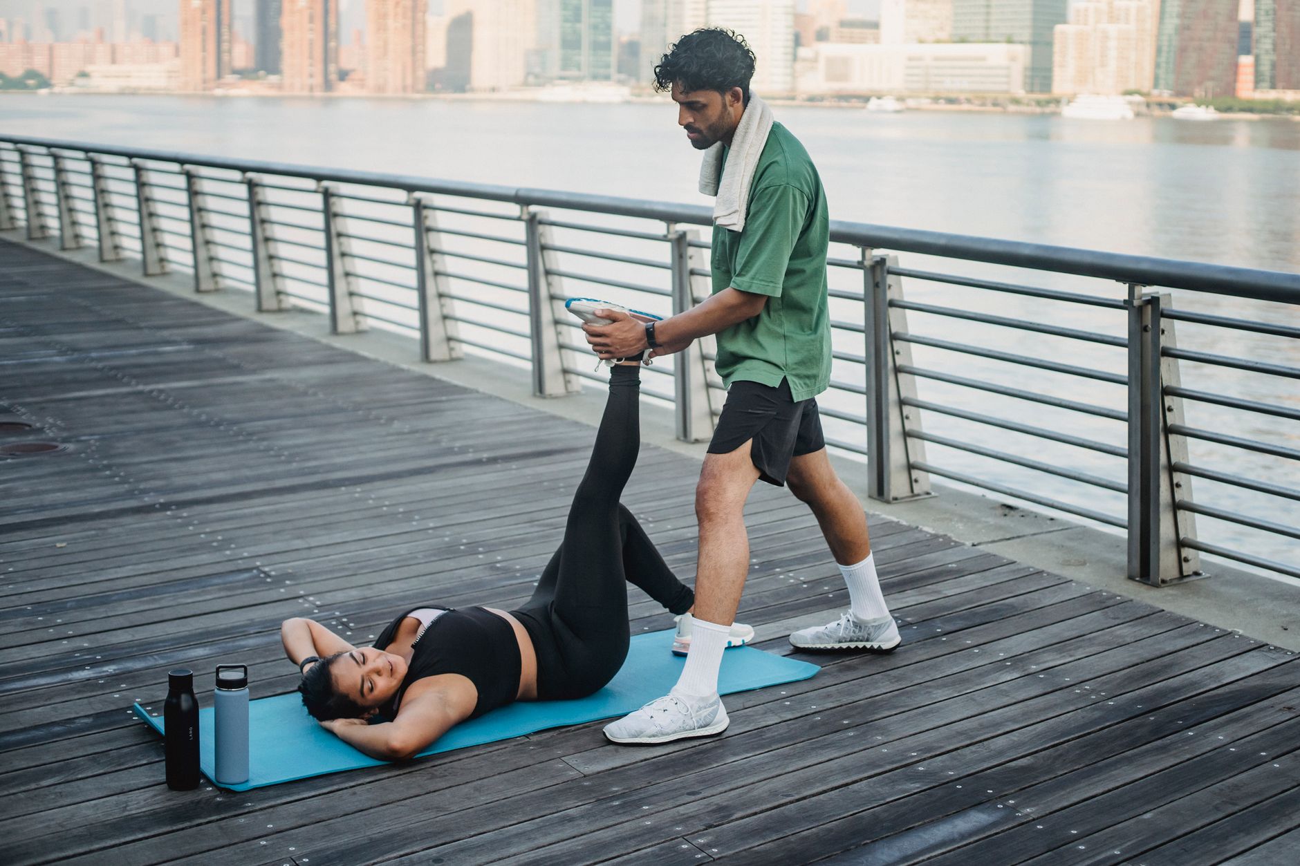 A woman stretches on a yoga mat assisted by a man, beside a riverfront railing. — Lemon And Sodium Bicarbonate As Teeth White