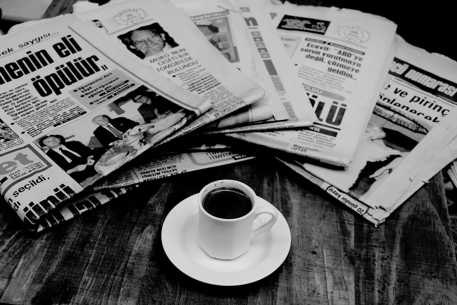A cup of Turkish coffee sits on a wooden table next to a stack of newspapers. — Les conseils pour gérer son budget chez Betcl