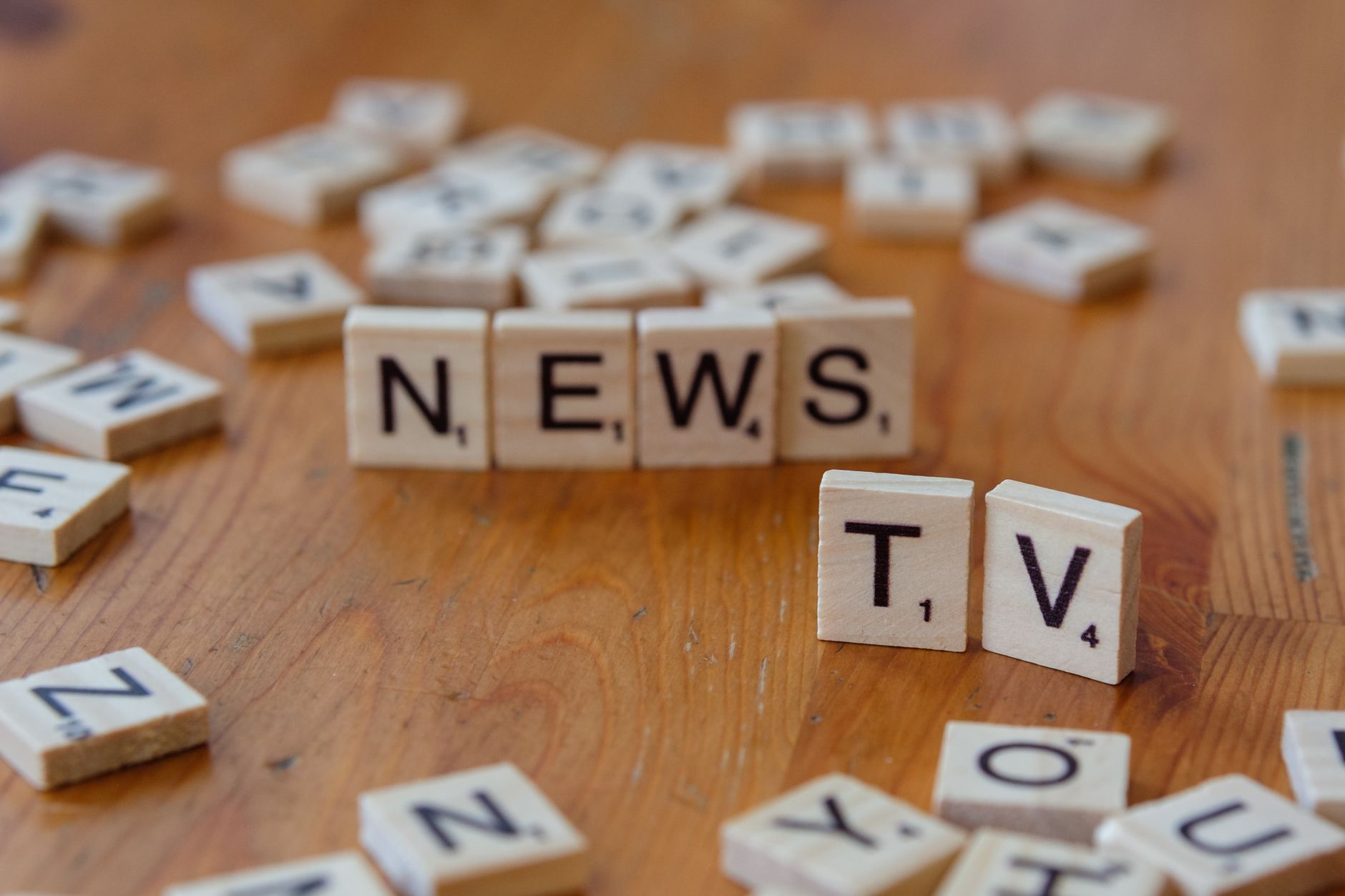 Close-up of Scrabble tiles spelling News and TV on a wooden surface. — Les fonctionnalités exclusives du site Gates of Olympu
