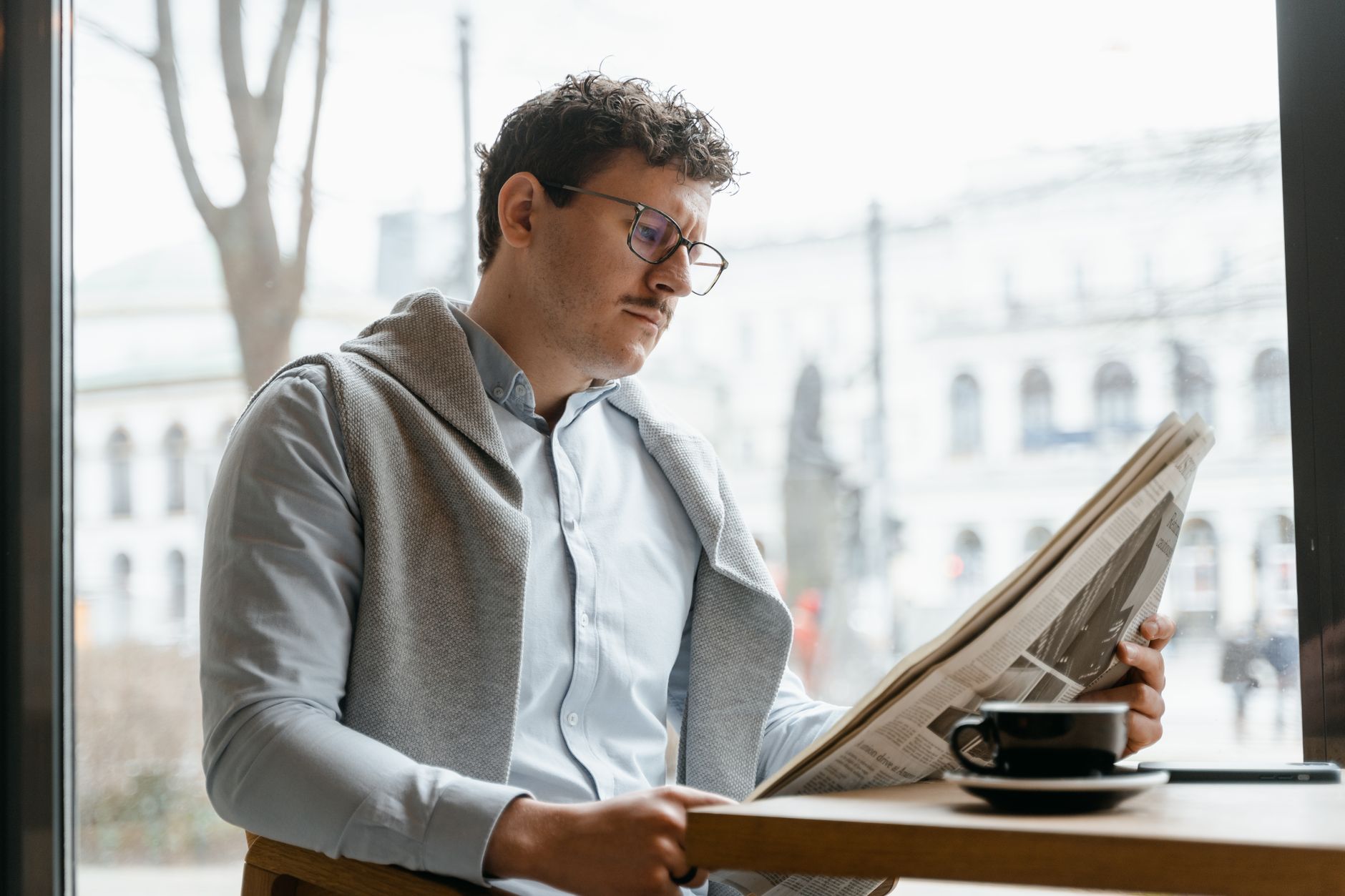 Adult man reads a newspaper by a café window, enjoying a coffee break indoors. — Malina Casino ou comment se démarquer dans l