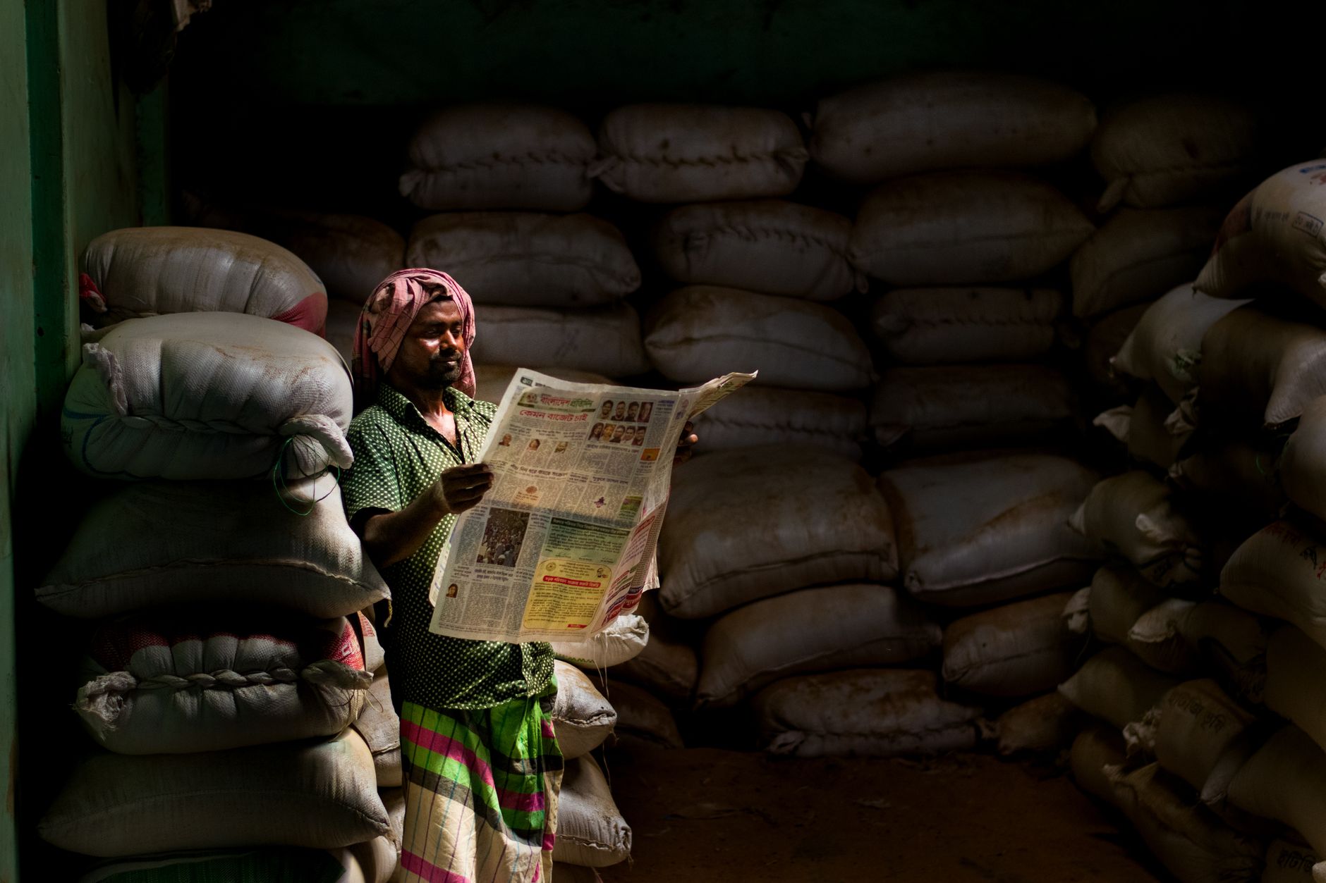 A man in traditional attire reads a newspaper in a dimly lit storeroom with stacked sacks. — Que savoir pour évaluer la quali