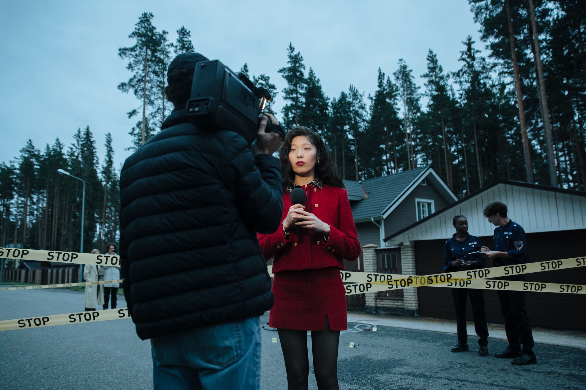 A female journalist reports live from an outdoor crime scene, flanked by police officers and media personnel. — Quel est le c