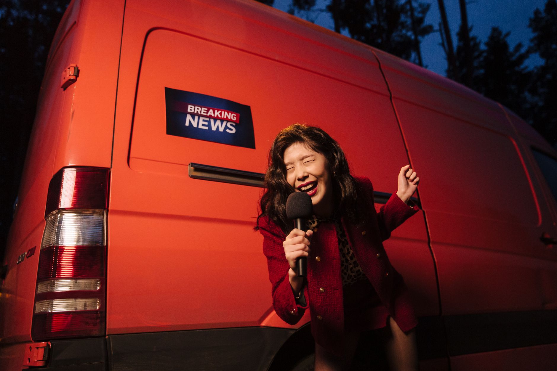 Asian woman reporter energetically broadcasting with a microphone in front of a news van at night. — Turbowins et la gestion