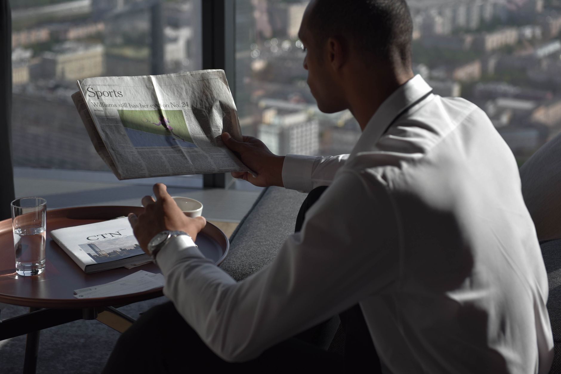 Businessman in office reading sports section, enjoying coffee with city view. — Welche Bonusangebote gibt es bei Lucky Seven
